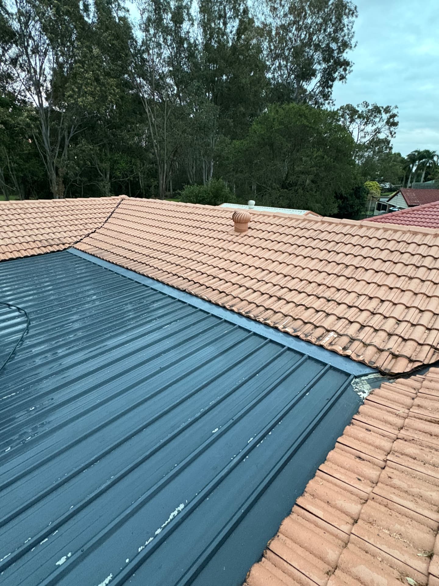 Completed metal fly-over roof with new transition flashing against a tiled roof in Manly, Brisbane